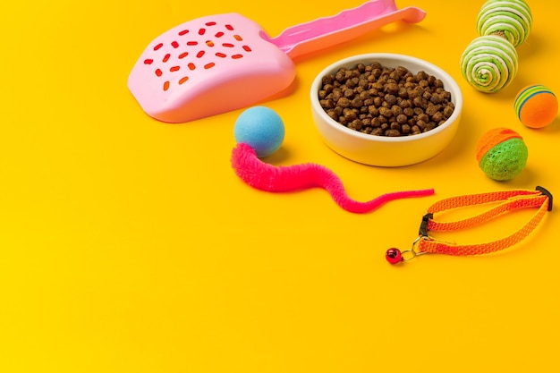 Kattenbak met droog voedsel en speelgoed op gele achtergrond studio opname