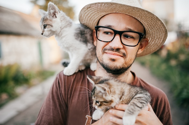 Kattenliefhebber. Jonge gelukkige jongen die in strohoed twee katjes houdt bij aard.