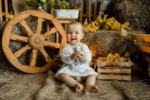 Kaukasisch babymeisje in een witte linnen jurk zit onder de pasen-zone met eendjes. viering van het heldere pasen