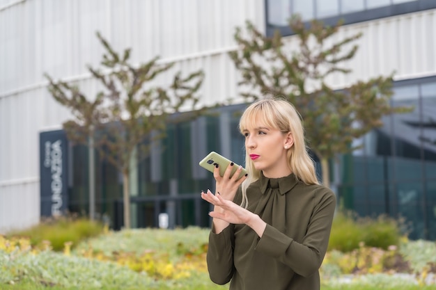 Kaukasisch blond ondernemersmeisje in een bedrijvenpark dat een audionotitie verzendt met de telefoon