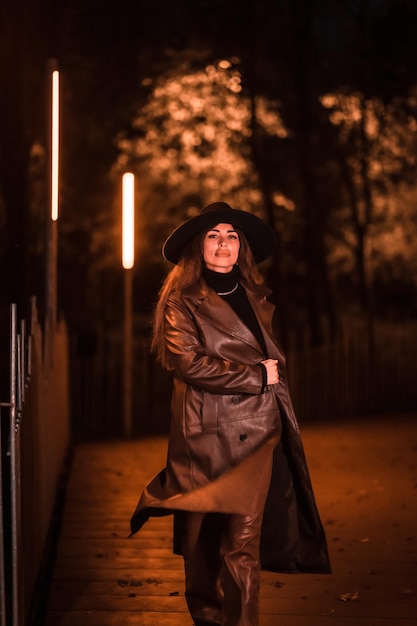 Kaukasisch brunette meisje met hoed die 's nachts in een park loopt. Winteravondmode