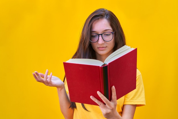 Kaukasisch jong meisje dat met lang donkerbruin haar een rood boek leest met verbaasde uitdrukking