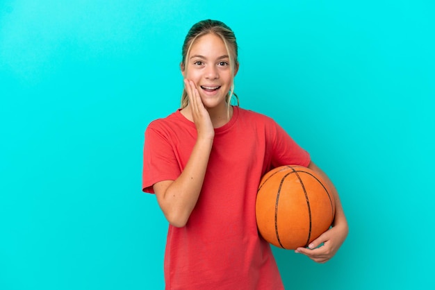 Kaukasisch meisje dat basketbal speelt geïsoleerd op blauwe achtergrond met verrassing en geschokte gezichtsuitdrukking
