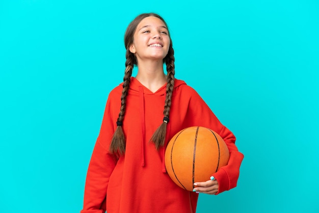 Kaukasisch meisje dat basketbal speelt geïsoleerd op een blauwe achtergrond lachen