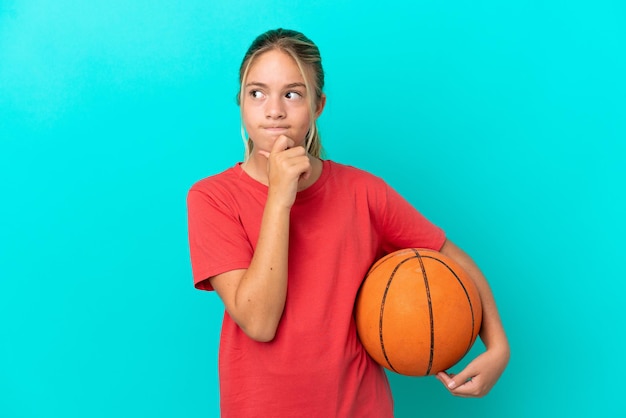 Kaukasisch meisje dat basketbal speelt geïsoleerd op een blauwe achtergrond met twijfels en denken