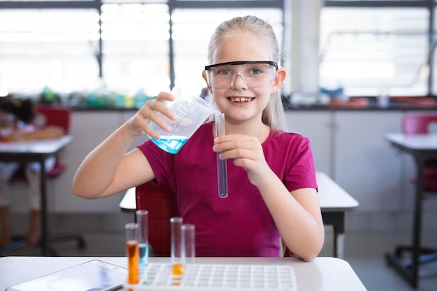 Kaukasisch meisje dat chemische stof uit bekerglas in reageerbuis giet in de wetenschapsklas in het laboratorium