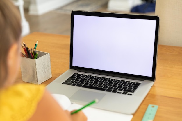 Kaukasisch meisje dat thuis een laptop met een leeg scherm gebruikt. huishoudelijke levensstijl en online onderwijs tijdens de covid-19-pandemie concept.