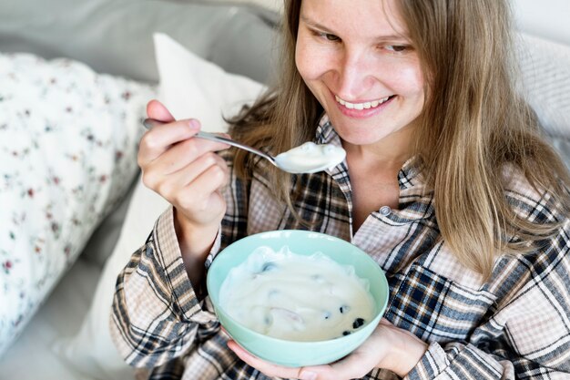 Kaukasisch meisje dat yoghurt op bed eet