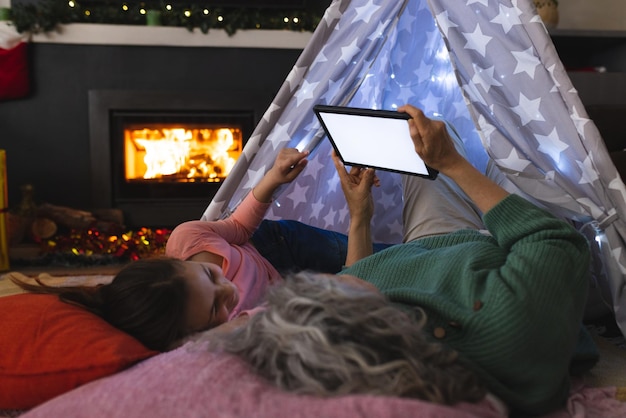 Kaukasisch meisje en grootmoeder brengen samen tijd door in de tipi en gebruiken tablet. Kerstmis, familietijd en feestconcept.