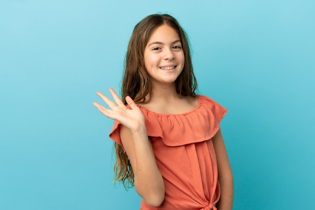 Kaukasisch meisje geïsoleerd op blauwe achtergrond saluerend met de hand met gelukkige uitdrukking happy