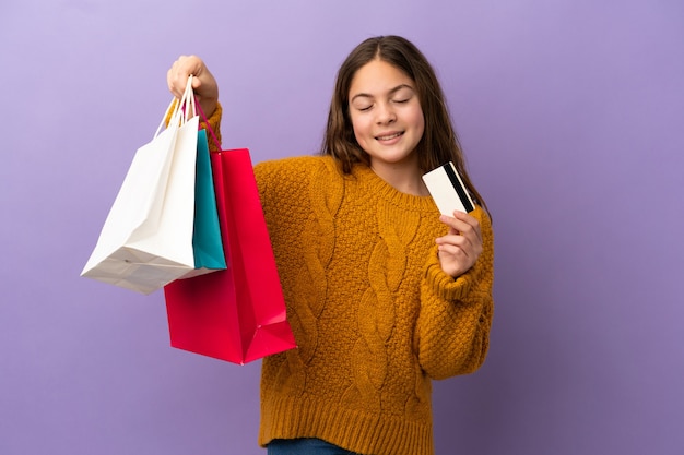 Kaukasisch meisje geïsoleerd op een paarse achtergrond met boodschappentassen en een creditcard