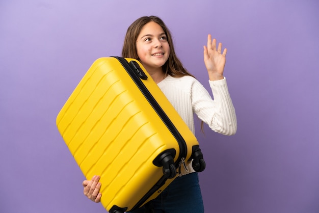 Kaukasisch meisje geïsoleerd op paarse achtergrond in vakantie met reiskoffer en saluting