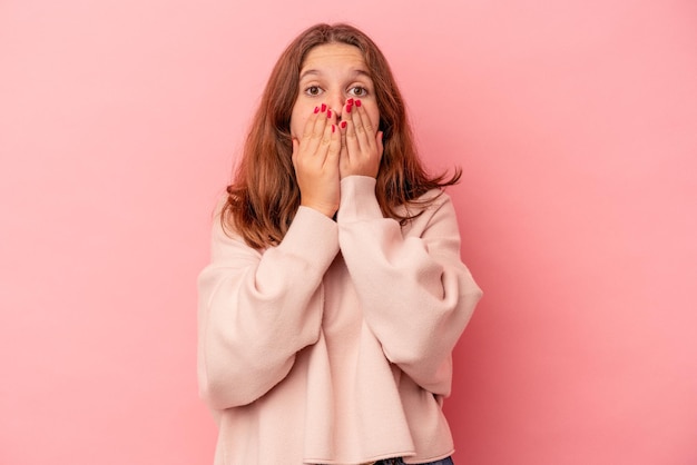 Kaukasisch meisje geïsoleerd op roze achtergrond geschokt, mond bedekken met handen, angstig om iets nieuws te ontdekken.