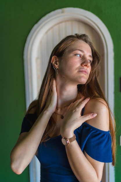 Kaukasisch meisje in een blauwe jurk naast een witte deur van een verticale foto van een groen huis