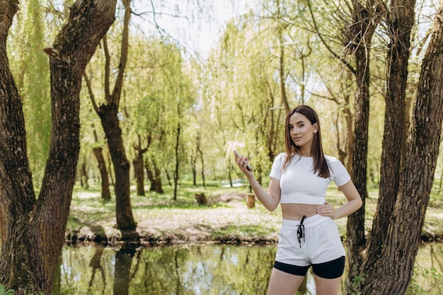 Kaukasisch meisje in sportoutfit lacht en gebruikt haar smartphone in een groen park