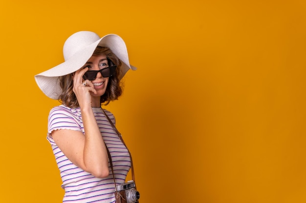 Kaukasisch meisje in toeristisch concept met een hoed en zonnebril genietend van zomervakantie gele achtergrond