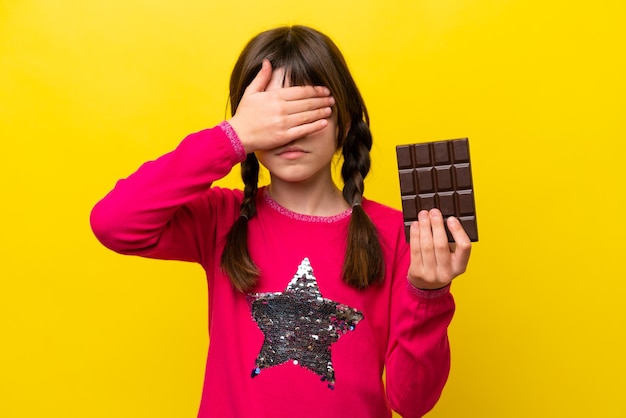 Foto kaukasisch meisje met chocolade geïsoleerd op een gele achtergrond die de ogen bedekt met de handen wil je iets niet zien?