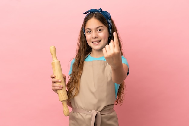 Kaukasisch meisje met een deegroller geïsoleerd op een roze achtergrond die komend gebaar doet