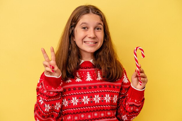Kaukasisch meisje met kerststok geïsoleerd op een gele achtergrond met nummer twee met vingers.