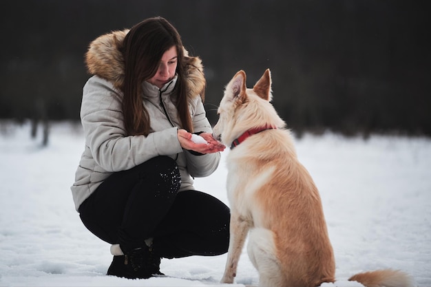 Kaukasisch meisje met lang haar zit in het winterpark met haar vriend witte pluizige hond Half ras