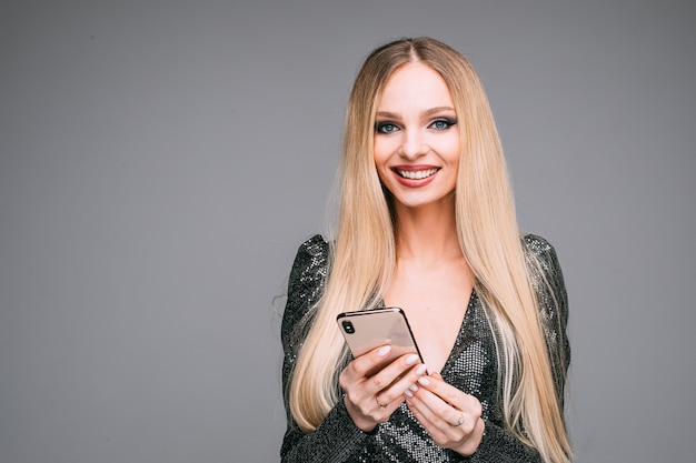 Kaukasisch meisje met lang wit haar en lichte make-up houdt smartphone in haar handen en glimlacht, foto geïsoleerd op een witte achtergrond