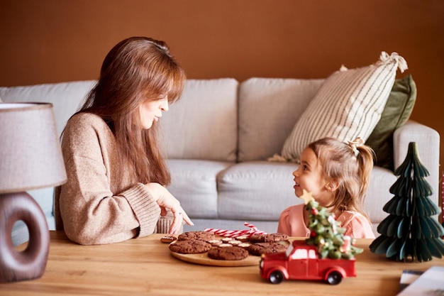 Kaukasisch meisje met moeder die smakelijke kerstkoekjes eet Gelukkig familiekerstconcept