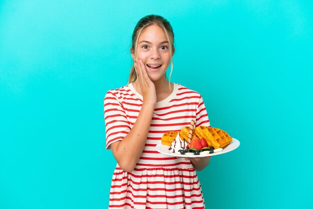 Kaukasisch meisje met wafels geïsoleerd op blauwe achtergrond met verrassing en geschokte gezichtsuitdrukking