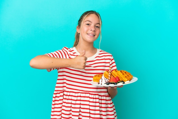 Kaukasisch meisje met wafels geïsoleerd op een blauwe achtergrond en geeft een duim omhoog gebaar