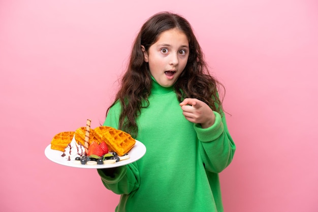 Kaukasisch meisje met wafels geïsoleerd op roze achtergrond verrast en wijzend naar voren