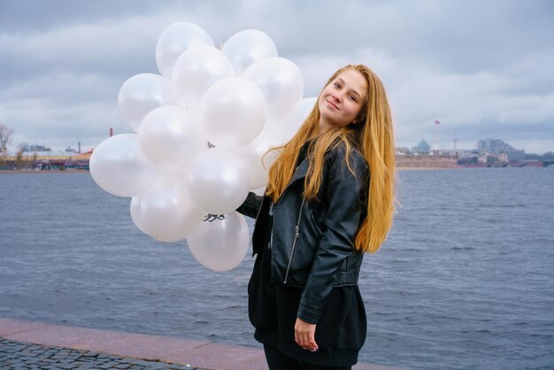 Kaukasisch meisje met witte ballonnen die 's middags bij de rivier aan de dijk van de stad staan in een ...