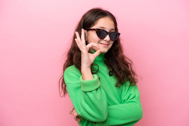 Kaukasisch meisje met zonnebril geïsoleerd op roze achtergrond met ok teken met vingers