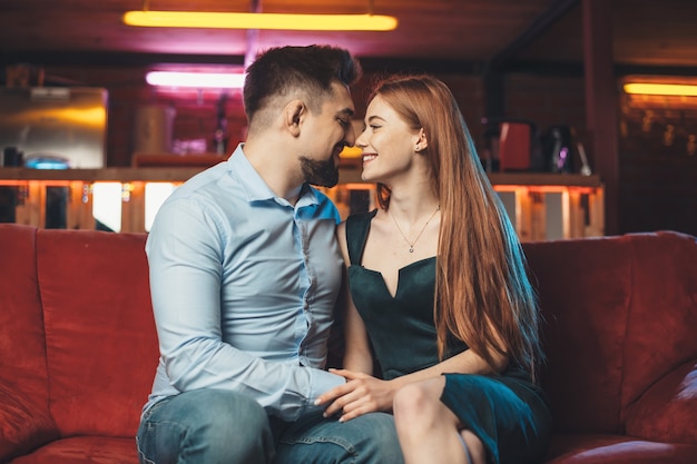 Kaukasisch paar lachend naar elkaar dating op Valentijnsdag op een rode bank in een cafetaria