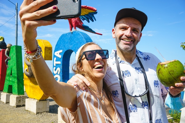 Kaukasisch paar van middelbare leeftijd dat een selfie maakt met een kokosnoot in hun hand naast Costa Rica-letters