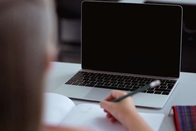 Kaukasisch schoolmeisje aan een bureau in de klas die laptop schrijft en gebruikt, met kopieerruimte op het scherm