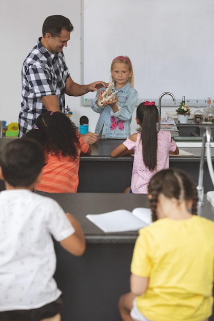 Kaukasisch schoolmeisje houdt een schedel in haar handen en laat deze zien aan andere zittende schoolkinderen