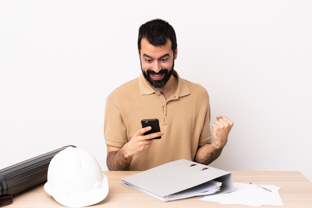 Kaukasische architect man met baard in een tafel verrast en het verzenden van een bericht