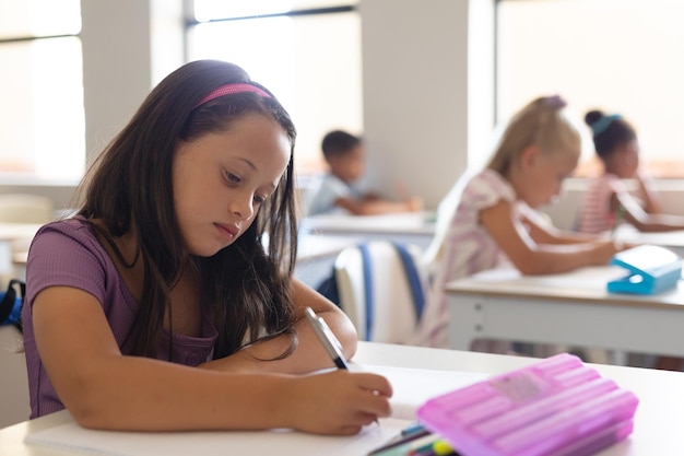 Kaukasische basisscholier schrijft op een boek terwijl ze aan het bureau in de klas leert