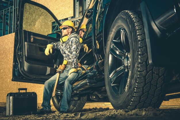 Foto kaukasische bouwwerknemer in de dertig ontspant na een zware werkdag werknemer en zijn zwarte pick-up industriële thema