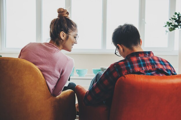 Kaukasische business paar werken vanuit huis op de laptop in de fauteuil terwijl het dragen van een bril met behulp van laptop