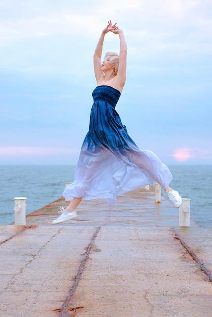 Kaukasische gelukkige blonde vrouw met kort haar die bij de zee springt in de zonsopgang