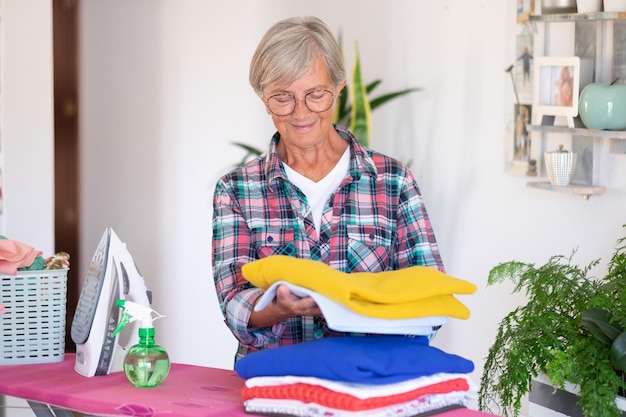 Kaukasische glimlachende hogere vrouw die kleren thuis op strijkplank strijkt