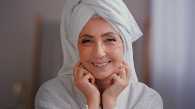 Kaukasische glimlachende vrouw in badjas met handdoek op hoofd met het glimlachen van vlekken van huidverzorgingsogen