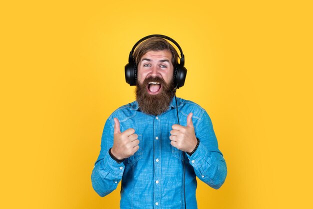 Kaukasische hipster met baard en stijlvol haar in headset met duim omhoog succes