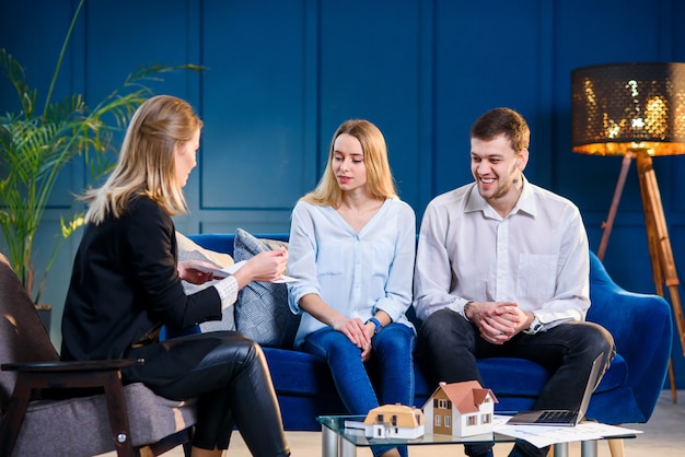 Kaukasische jonge man en vrouw op de ontmoeting met makelaar in onroerend goed, binnenhuisarchitect, decorateur.