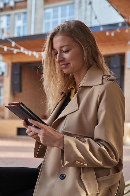 Kaukasische jonge vrouw in jas die tablet buitenshuis gebruikt op een zonnige dag die ebook leest