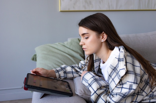 Kaukasische jonge vrouw kijkt naar de tablet die op de bank ligt