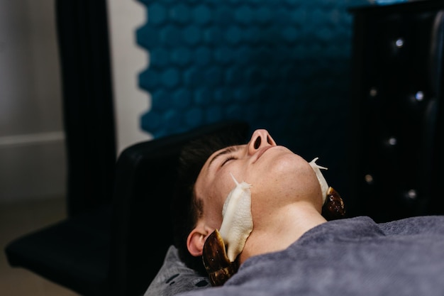 Kaukasische jongeman die slakkenmassage ontvangt Gezichtstherapie en verzorging met slakken in spa salon Moderne cosmetologische procedure voor huidverjonging