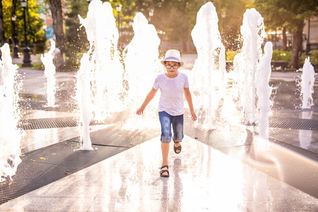 Kaukasische jongetje in hoed spelen en plezier maken met water in de fontein in het zonnige zomer park