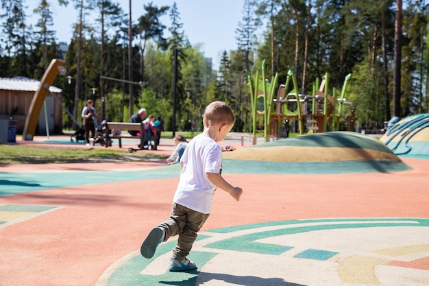 Kaukasische kleine jongen loopt op een zonnige dag door het grondgebied van de speeltuin buiten.