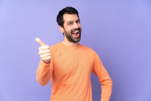 Kaukasische knappe man over paarse muur met duimen omhoog omdat er iets goeds is gebeurd